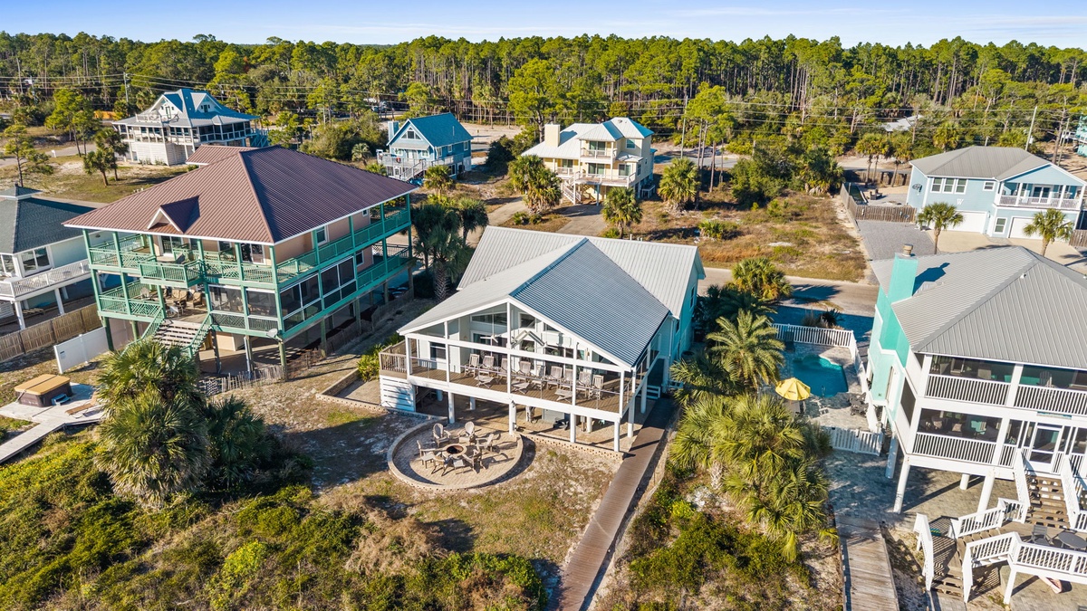 Coastal vacation homes nestled among palm trees with wooden decks and fire pit, surrounded by natural forest landscape.