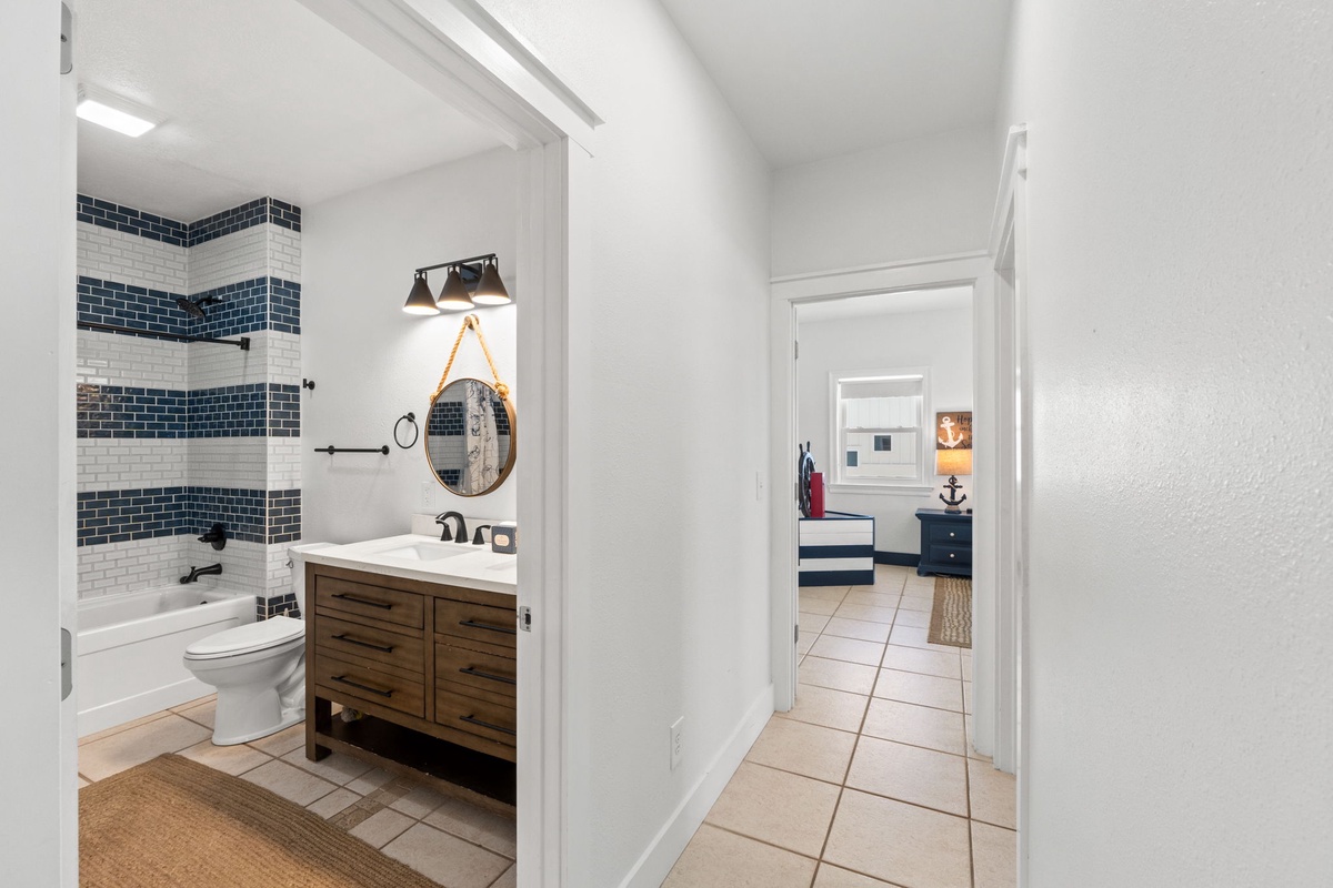 Your private bathroom features nautical-inspired blue and white tilework, a warm wooden vanity, and a soothing tub—perfect for unwinding after a day by the shore.