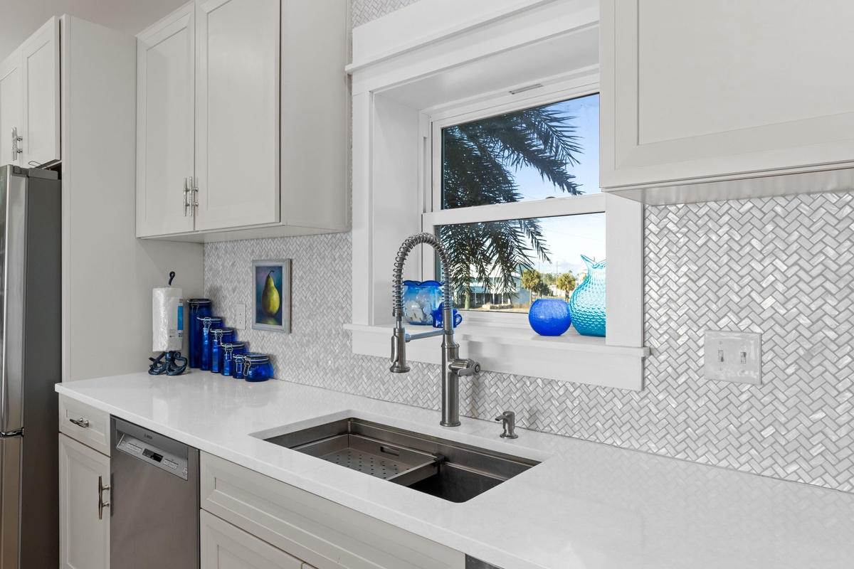 Your fully equipped kitchen features elegant white cabinetry and modern appliances, perfect for preparing meals while enjoying tropical views through the window.