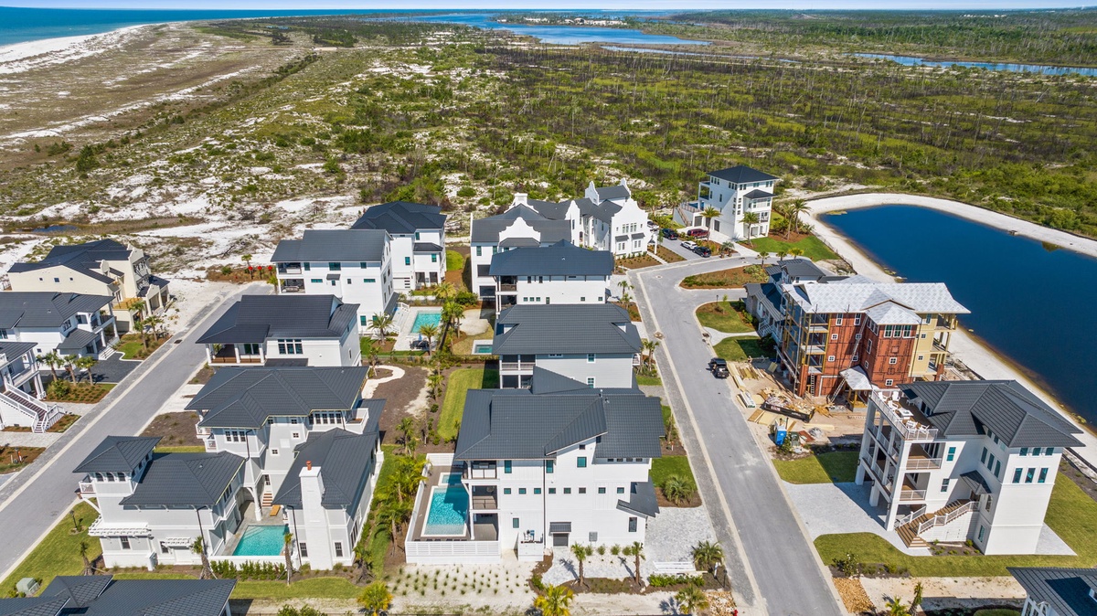 Aerial view of a coastal residential community featuring modern vacation homes, private pools, and natural surroundings with beach and waterfront access nearby.