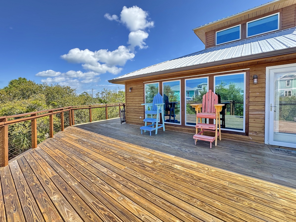 Spacious wooden deck with colorful Adirondack chairs perfect for morning coffee or evening relaxation overlooking lush coastal vegetation.