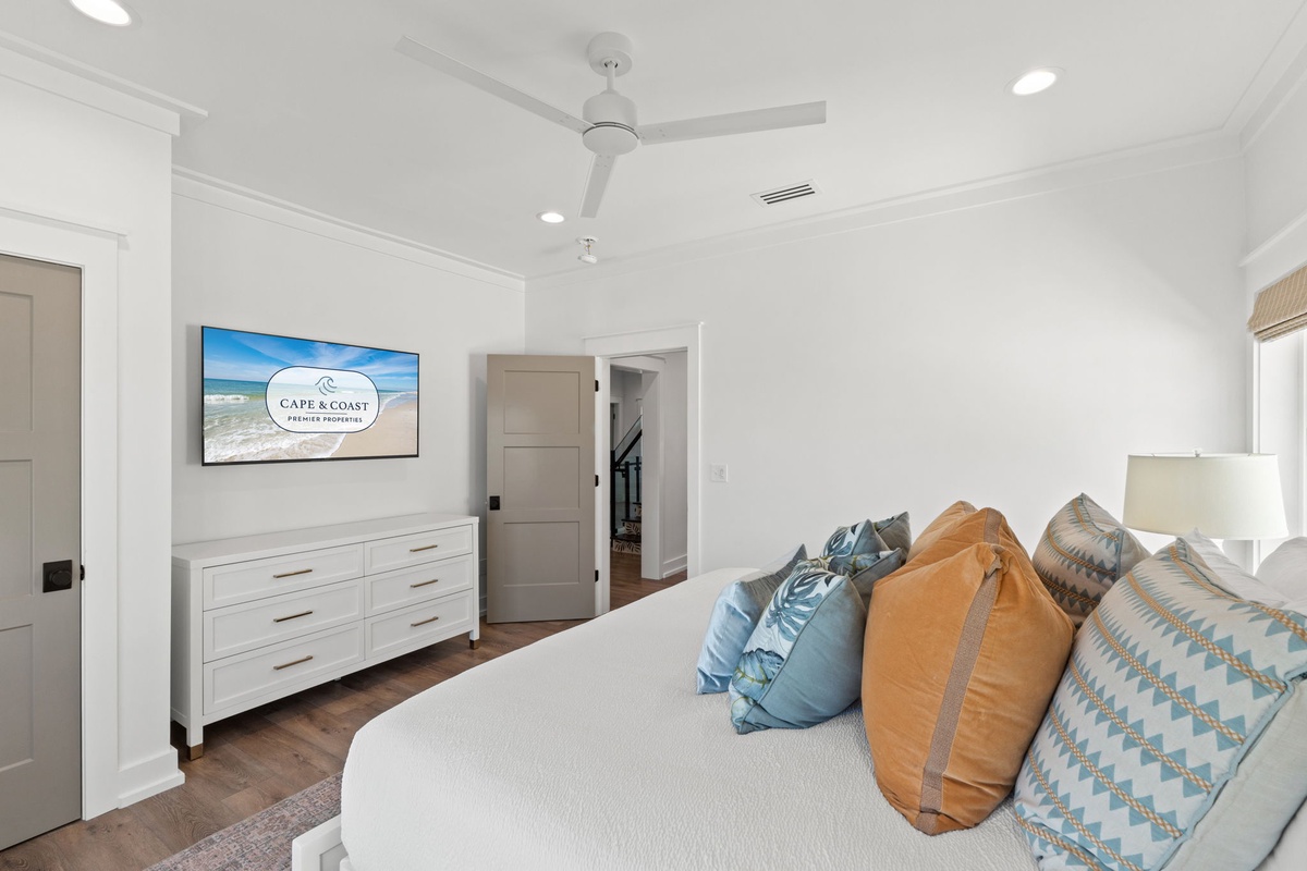 Relax in your serene bedroom with coastal touches, wall-mounted TV, and ceiling fan for perfect comfort.