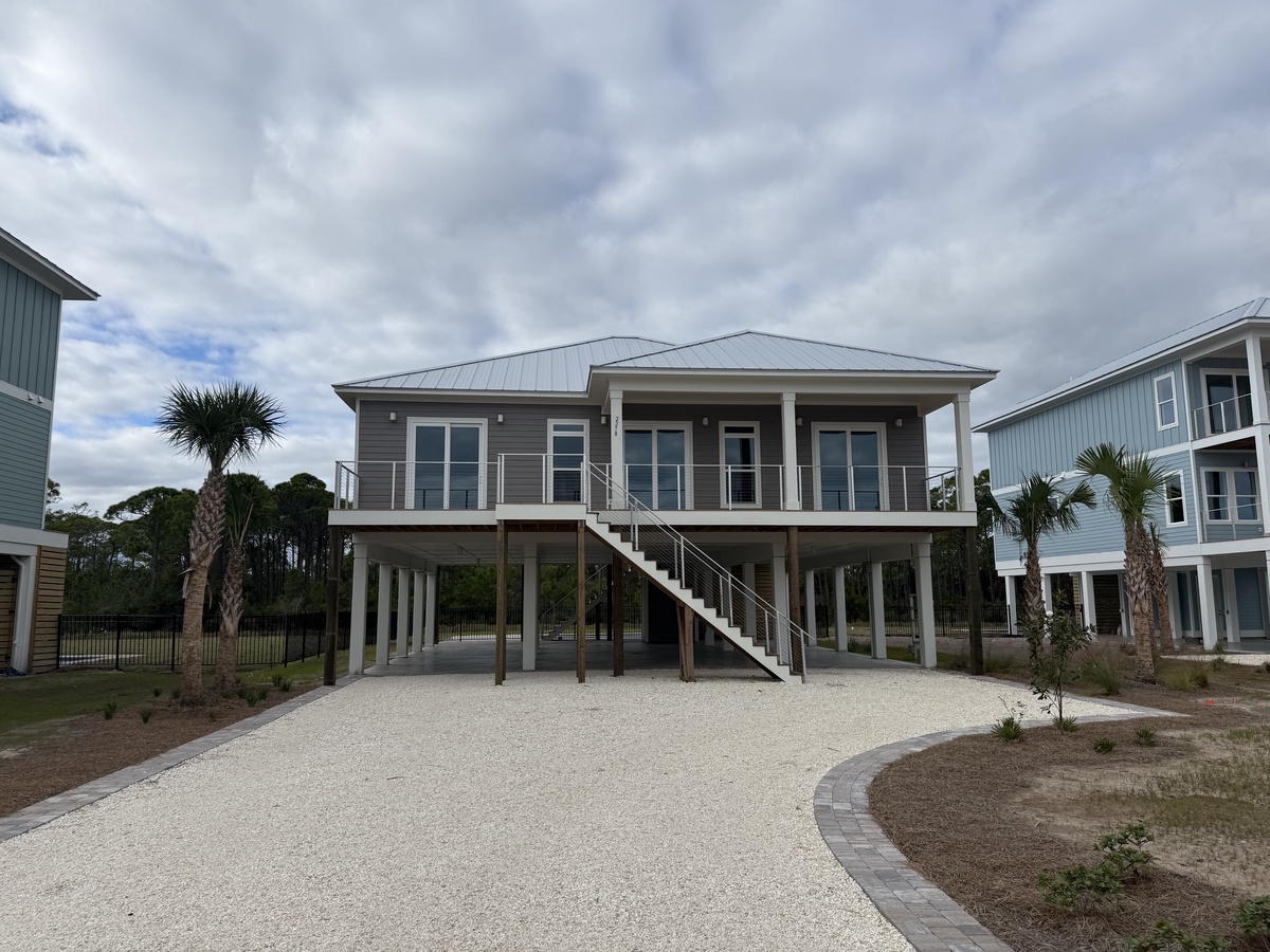 Modern coastal retreat elevated on stilts with covered parking and elegant staircase leading to wraparound porch and main living areas.