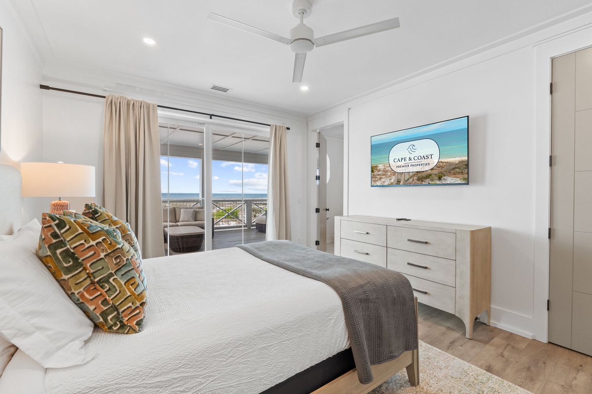 Your serene bedroom features ocean views through sliding doors, plus modern amenities like wall-mounted TV and ceiling fan for ultimate comfort.