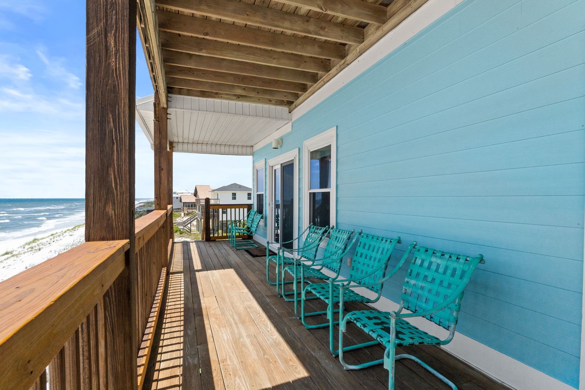 Coastal-front covered deck with vibrant turquoise seating overlooking sandy shores and ocean waves, perfect for relaxing mornings and sunset views.
