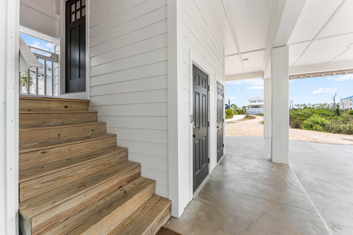 Bright entrance welcomes you with coastal charm—wooden steps lead to your elevated retreat above covered parking.