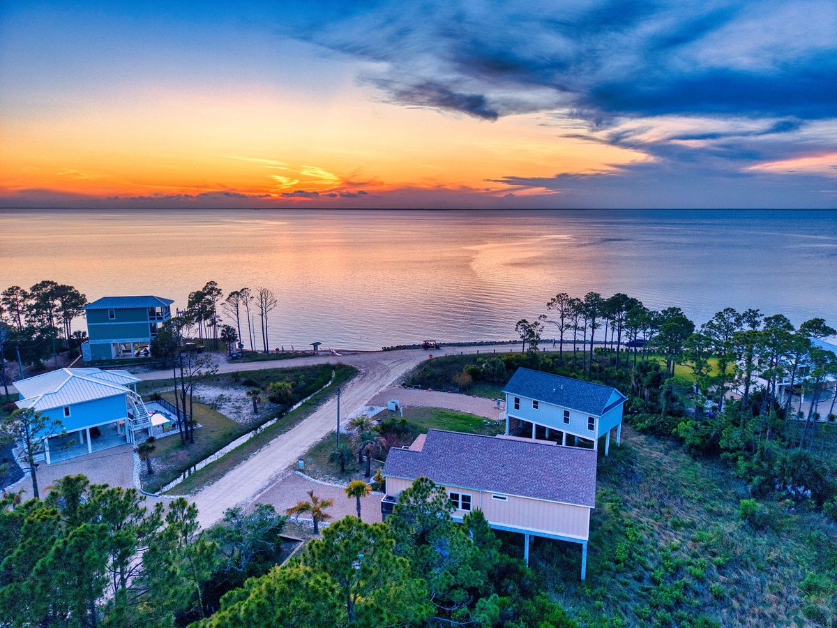 Aerial view of waterfront property nestled along scenic coastline at sunset, surrounded by natural landscape and neighboring homes.