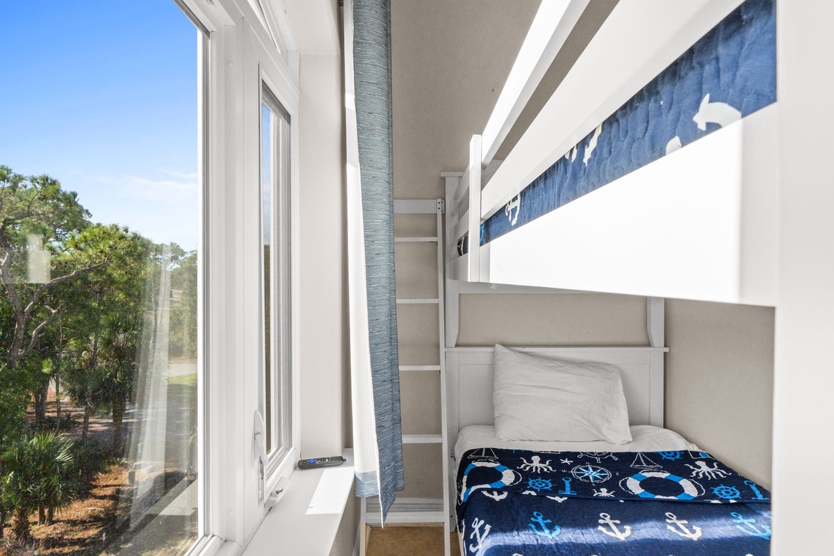 Drift off to sleep in your cozy maritime-themed bunk bed, with natural light streaming through large windows overlooking peaceful greenery.