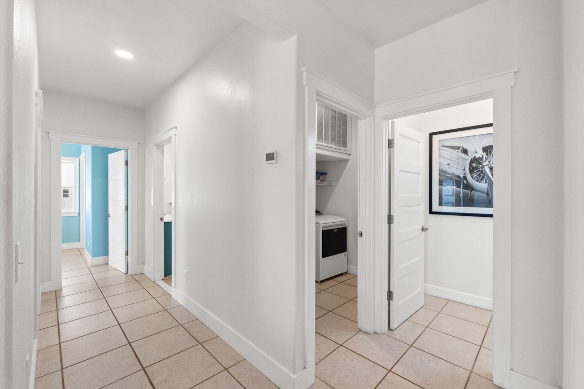 A welcoming hallway connects you to each space, featuring clean tile floors, crisp white walls, and glimpses of the fully-equipped kitchen and cozy bedrooms beyond.