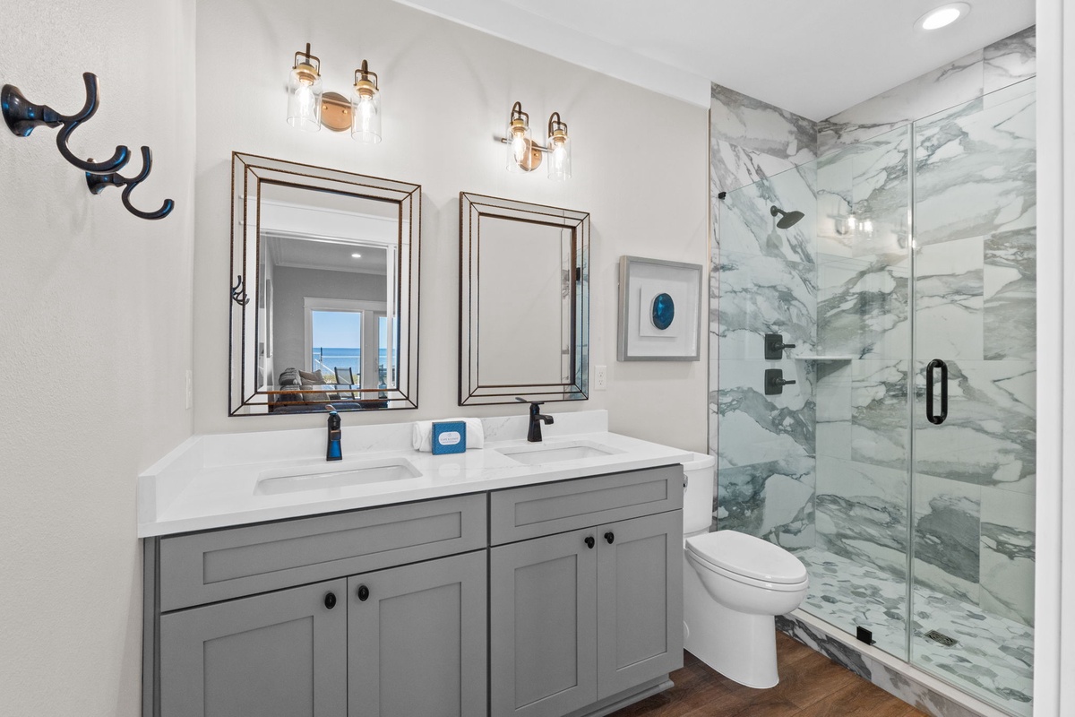 Unwind in your beautifully designed bathroom featuring a spacious walk-in shower with elegant marble walls, dual vanities for your convenience, and warm modern touches throughout.