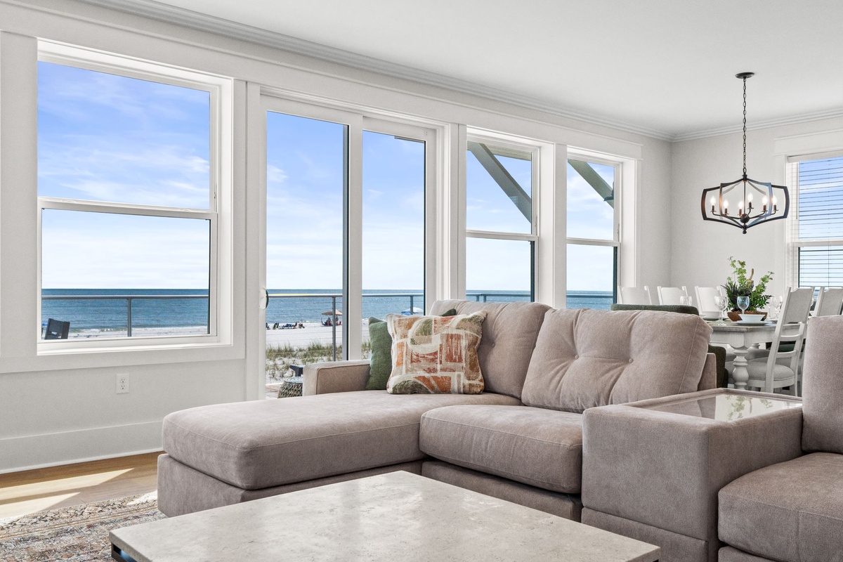 Sink into your plush sectional sofa and let the stunning ocean views wash over you. Sunlight streams through expansive windows, illuminating a serene, open living space perfect for unwinding after beach adventures.