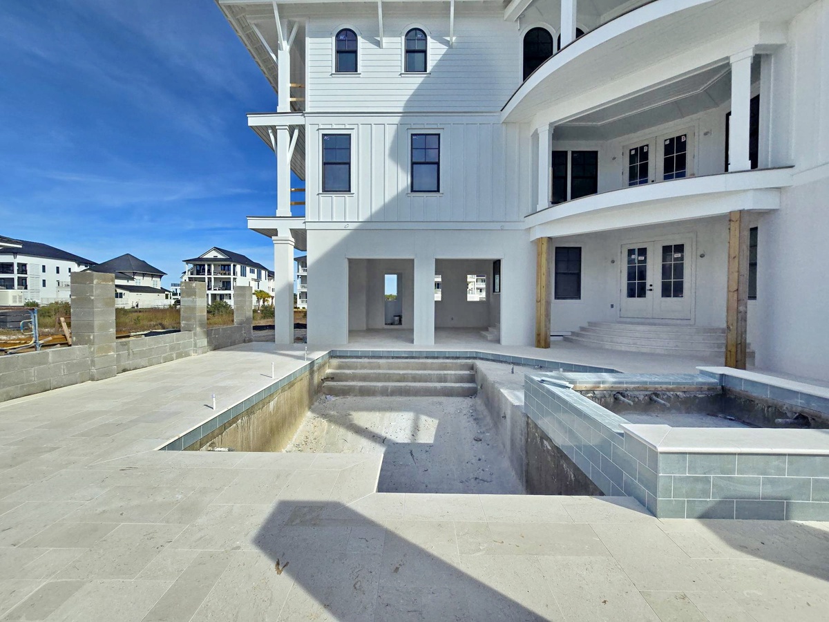 Modern coastal architecture frames an impressive pool area under construction, showcasing the luxury amenities awaiting completion.