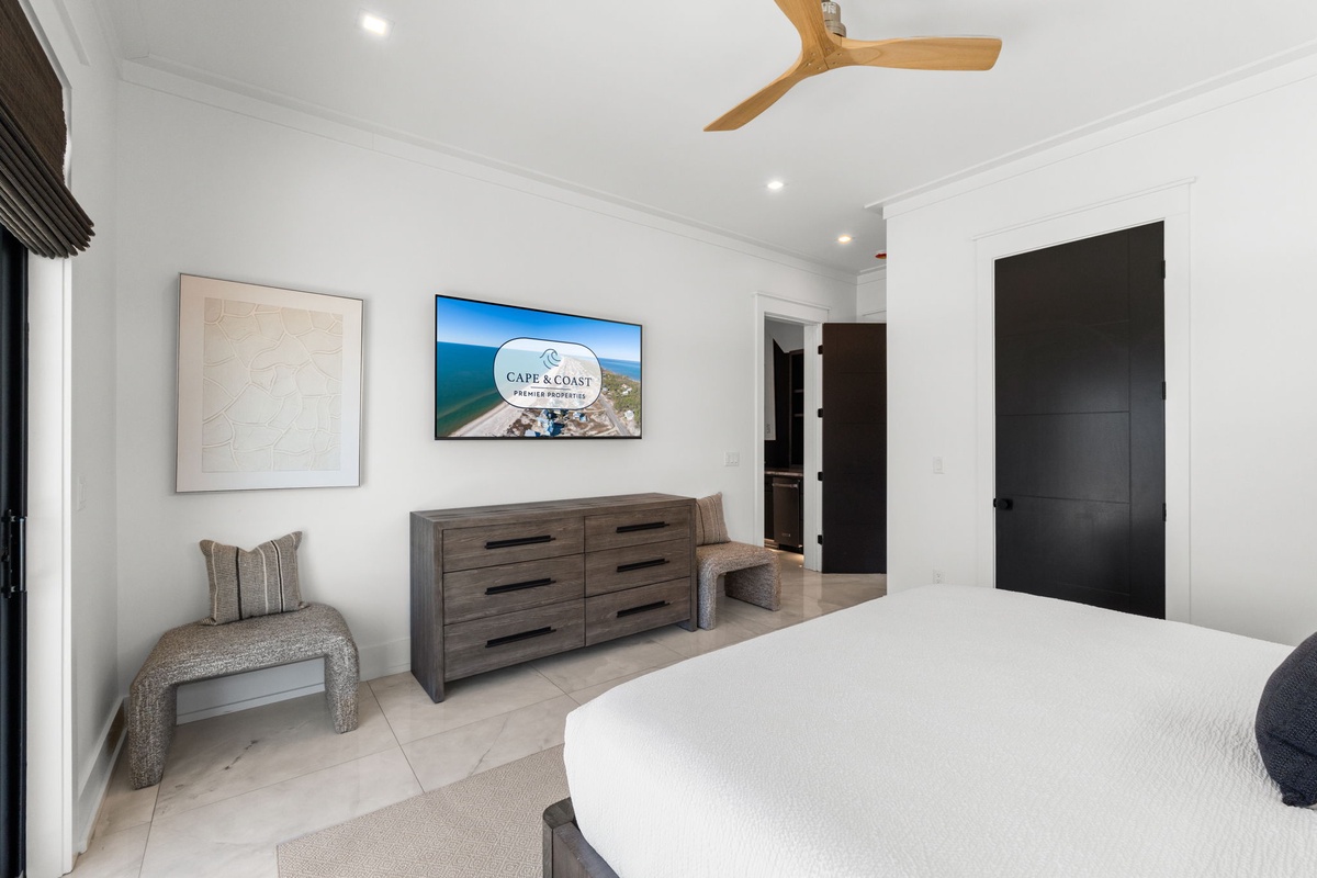 Unwind in your spacious bedroom featuring plush bedding, a mounted TV for entertainment, and a stylish ceiling fan to keep you cool and comfortable throughout your stay.