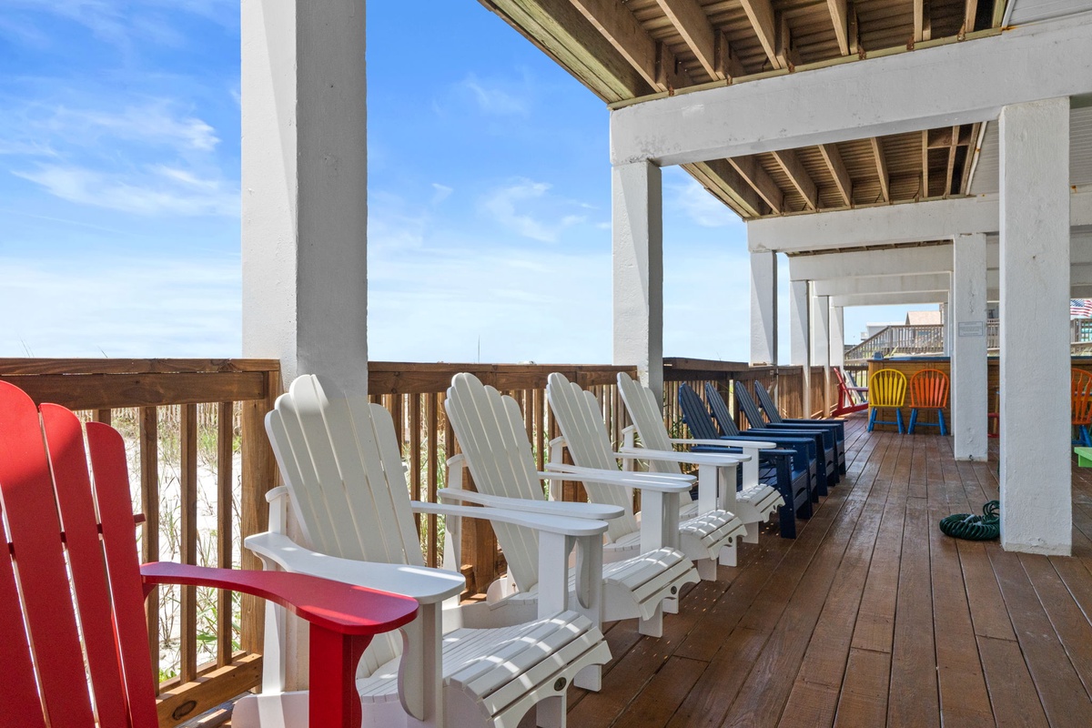 A row of classic Adirondack chairs lines this shaded deck, perfect for morning coffee or sunset views. The pergola overhead adds charm while offering relief from the sun, inviting you to slow down and soak in the coastal breeze.