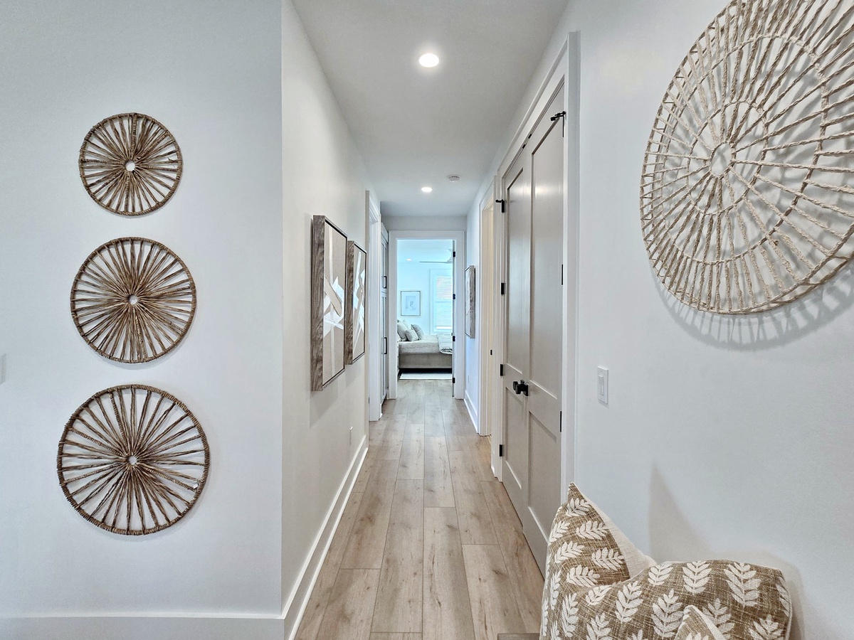 Wander through your stylish hallway, where natural woven art and warm wood floors guide you toward peaceful spaces ahead.