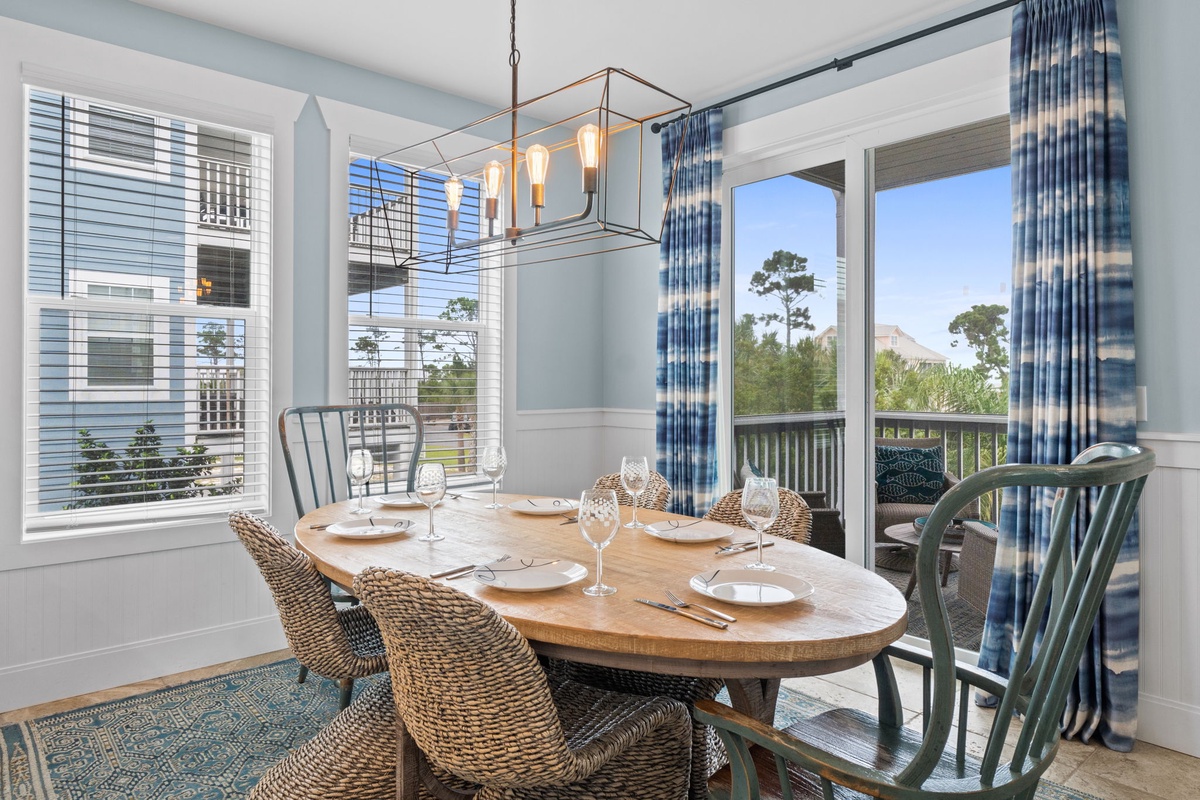 Step into your bright dining space where natural light floods through expansive windows, highlighting the coastal charm of woven seating and soft blue tones that set the perfect scene for memorable meals together.