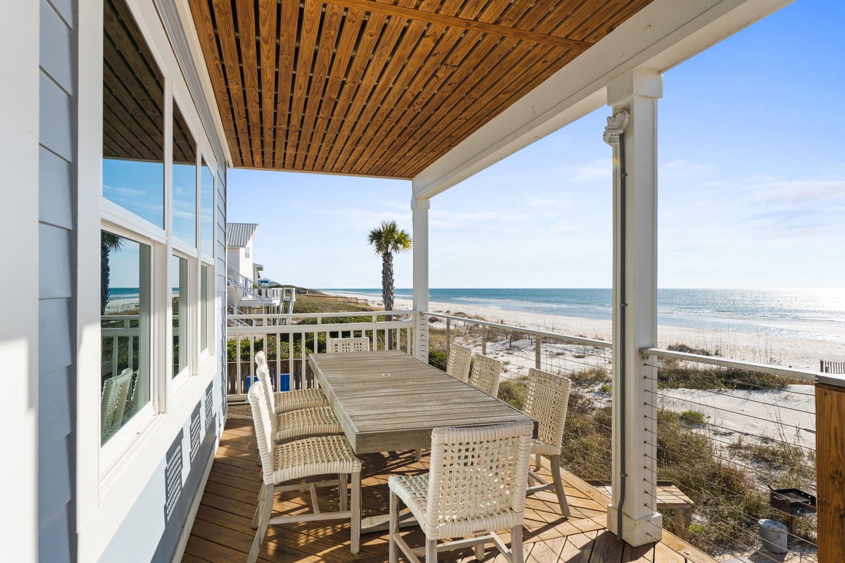 Expansive beachfront deck with dining table and woven chairs offering direct ocean views and coastal breeze access.