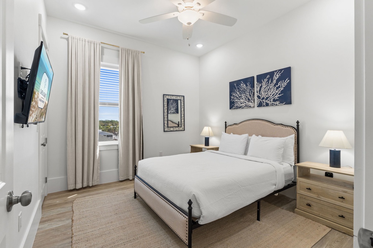 Unwind in your peaceful bedroom featuring a cozy queen bed, ceiling fan, and natural light streaming through elegant curtains.