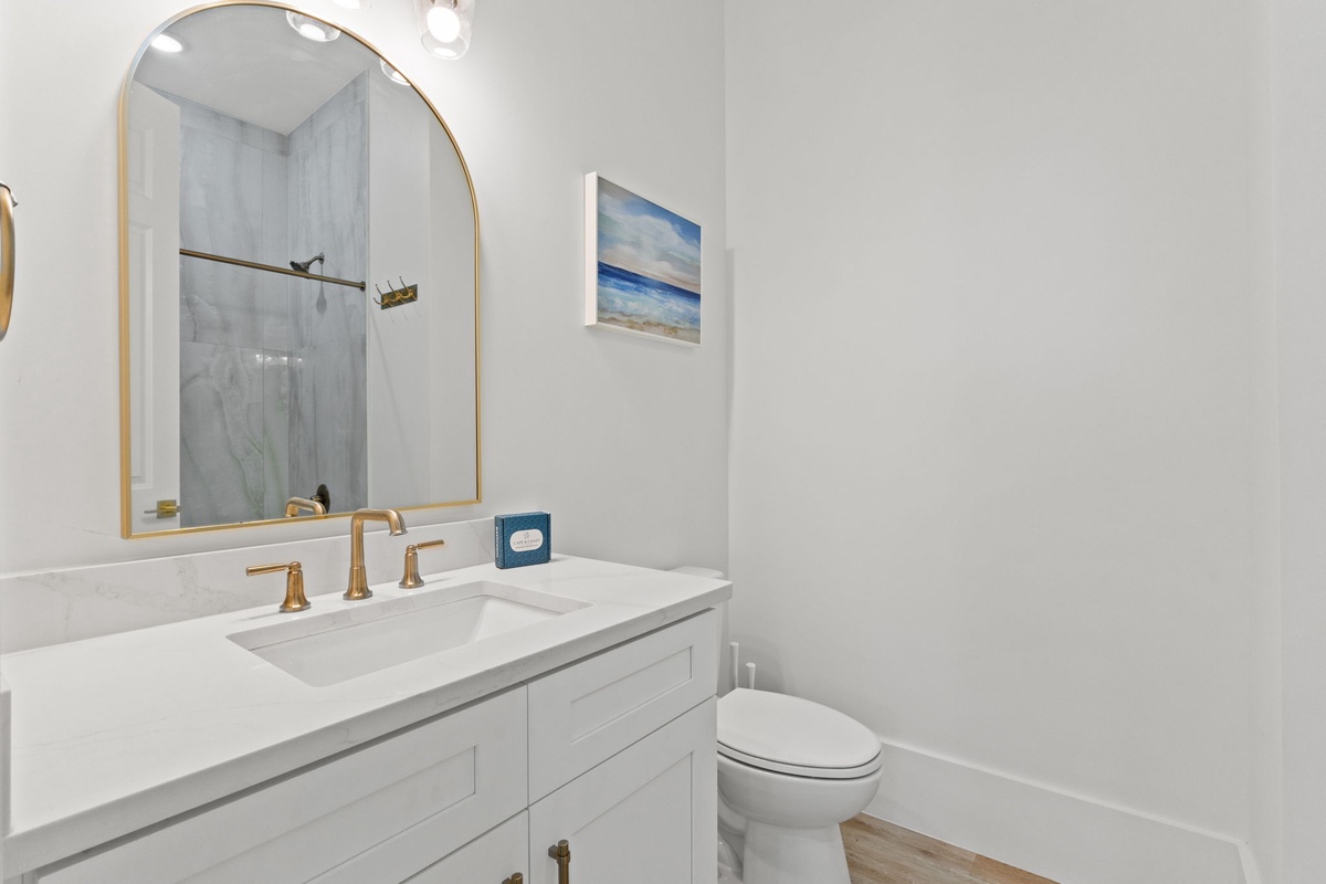 Freshen up in your elegant bathroom featuring crisp white marble counters, brass fixtures, and coastal artwork that creates a spa-like retreat.