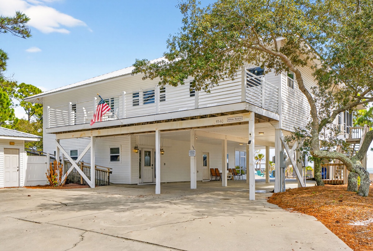 Charming coastal property featuring elevated design with covered parking and outdoor living spaces beneath mature shade trees.