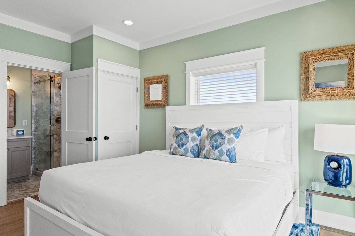 Relax in your peaceful coastal-inspired bedroom with soothing mint walls, plush white linens, and an elegant ensuite visible through the doorway—your perfect retreat after sun-filled days.