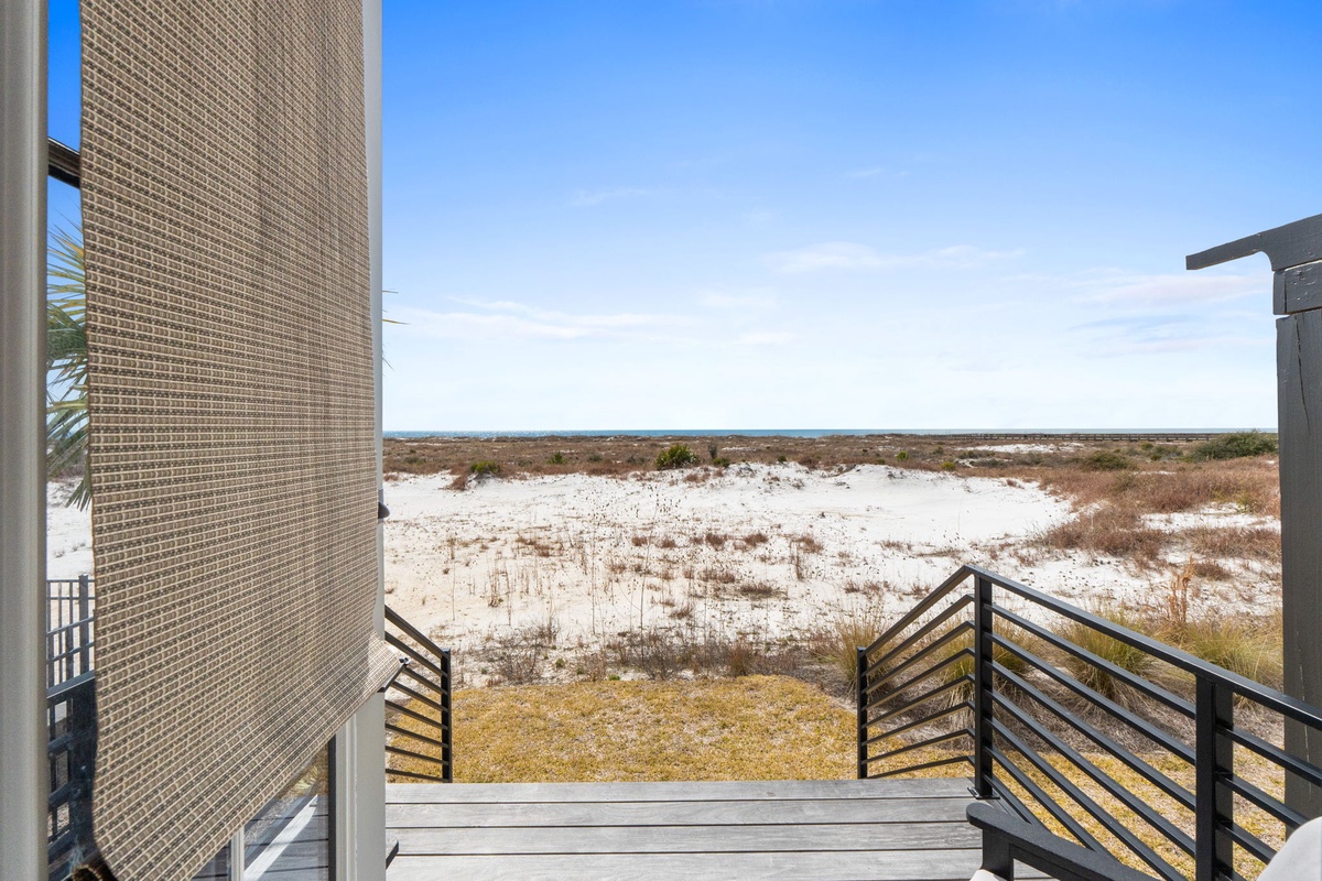 Balcony view overlooking pristine coastal dunes with native vegetation stretching toward the horizon under clear blue skies.
