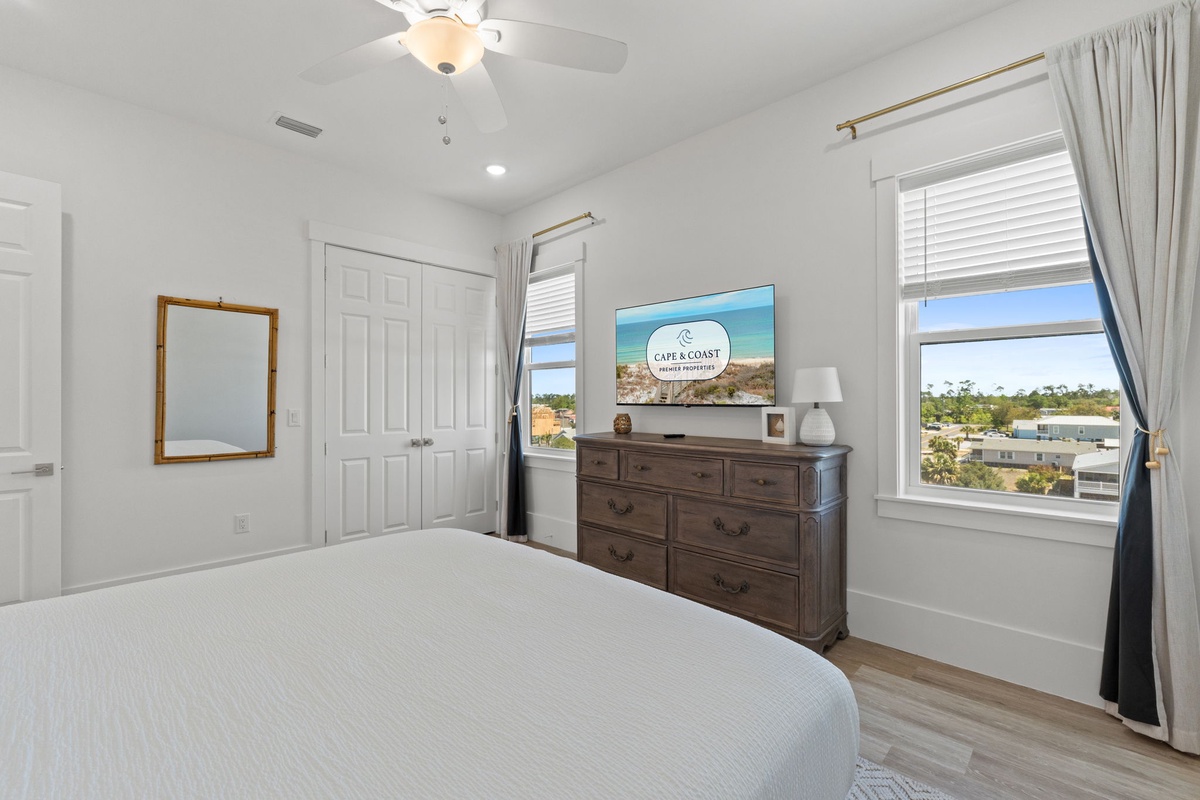 Your bright bedroom features a comfortable bed, spacious dresser with TV, and windows framing lovely neighborhood views.
