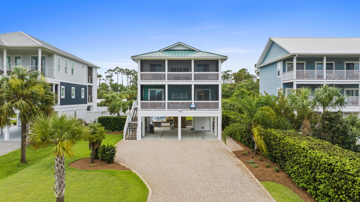 A charming coastal vacation home featuring a screened porch and elevated parking, surrounded by lush landscaping and palm trees in a peaceful residential neighborhood.