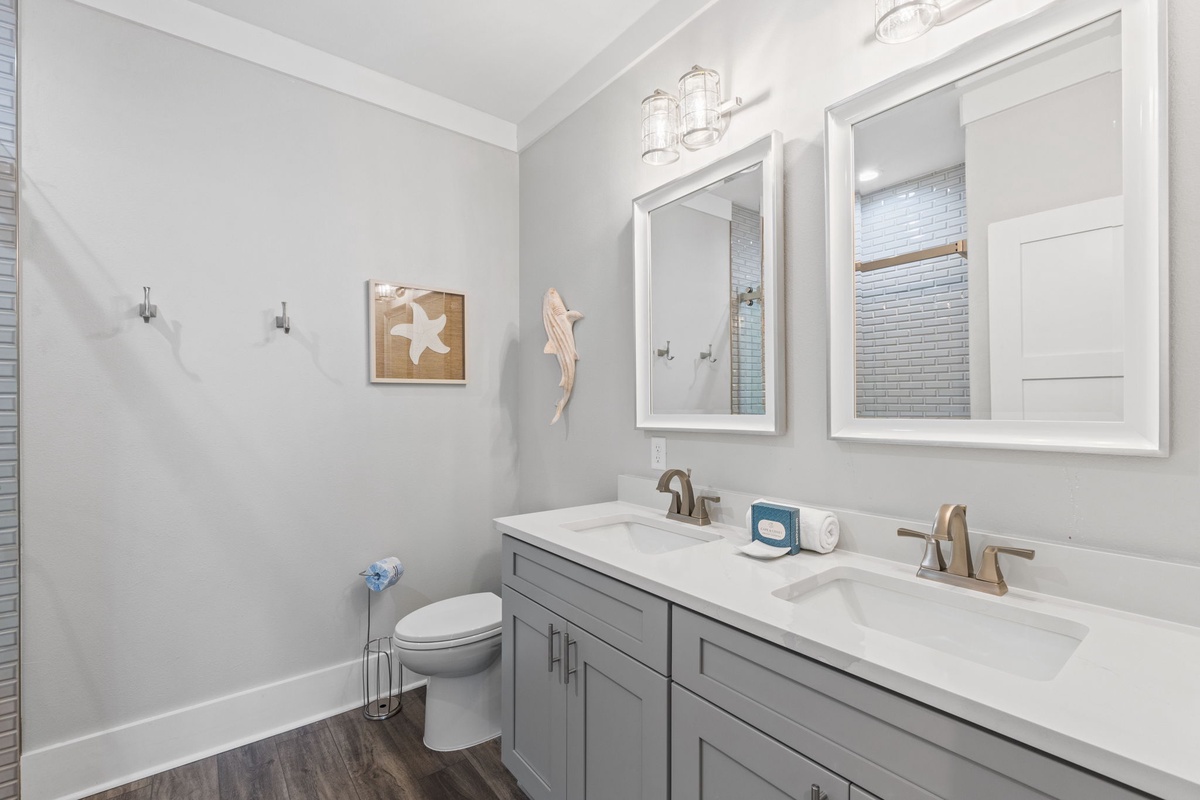 Your bright, coastal-inspired bathroom features dual sinks with ample counter space, a modern gray vanity, and charming beach-themed décor that sets a relaxing, seaside tone.