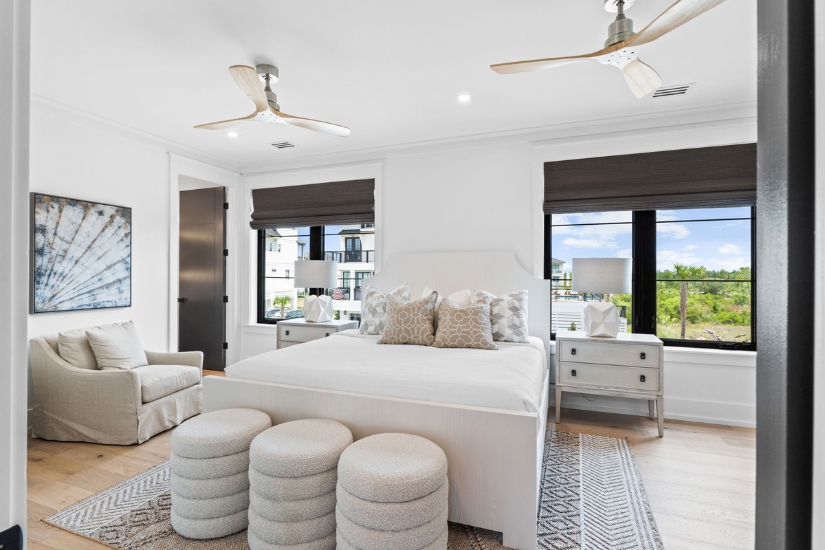 Drift off in this serene coastal bedroom with plush bedding, elegant furnishings, and calming natural light streaming through oversized windows.
