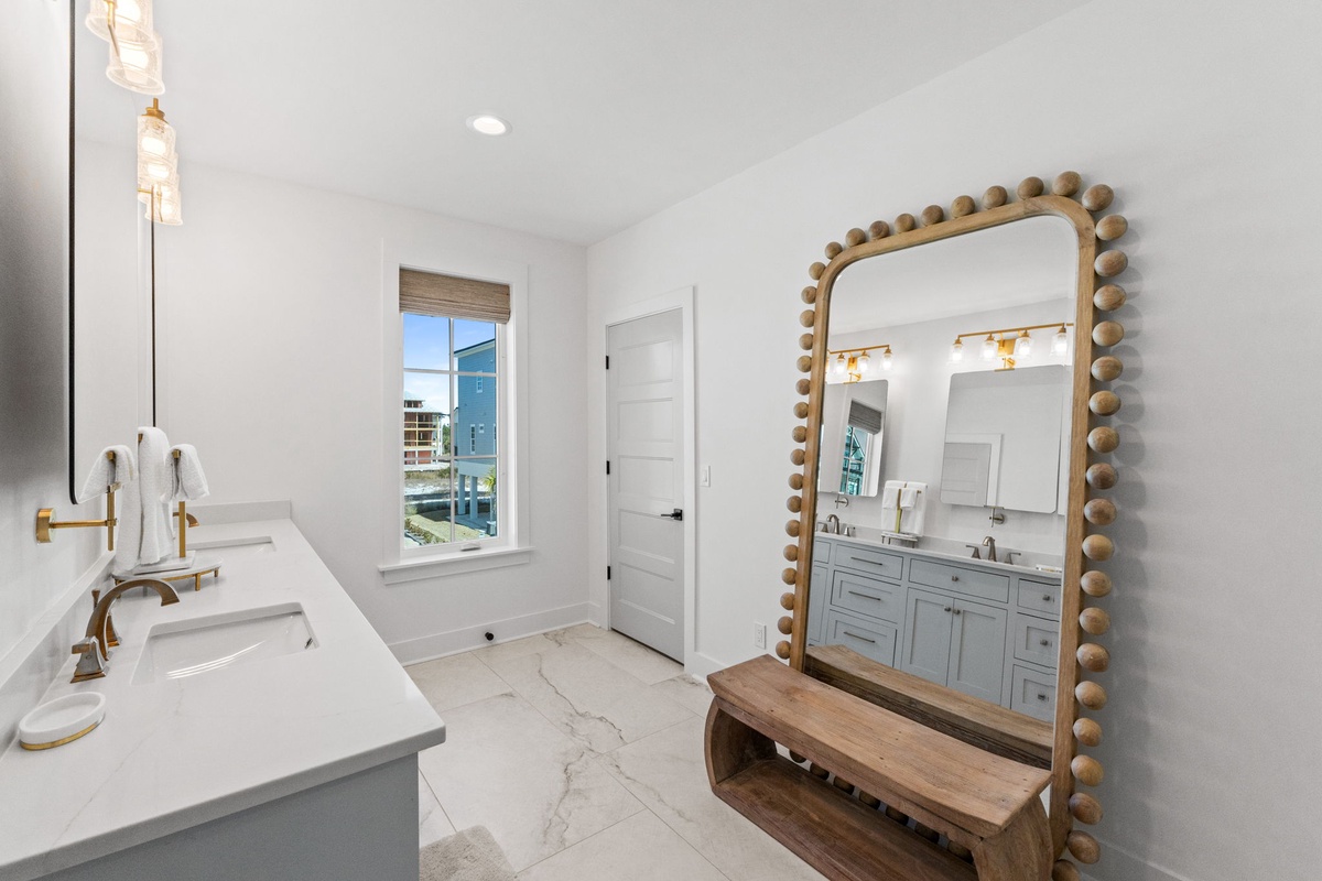 Your spacious bathroom features elegant marble countertops, gold fixtures, and a stunning statement mirror that perfectly complements the bright, airy atmosphere.