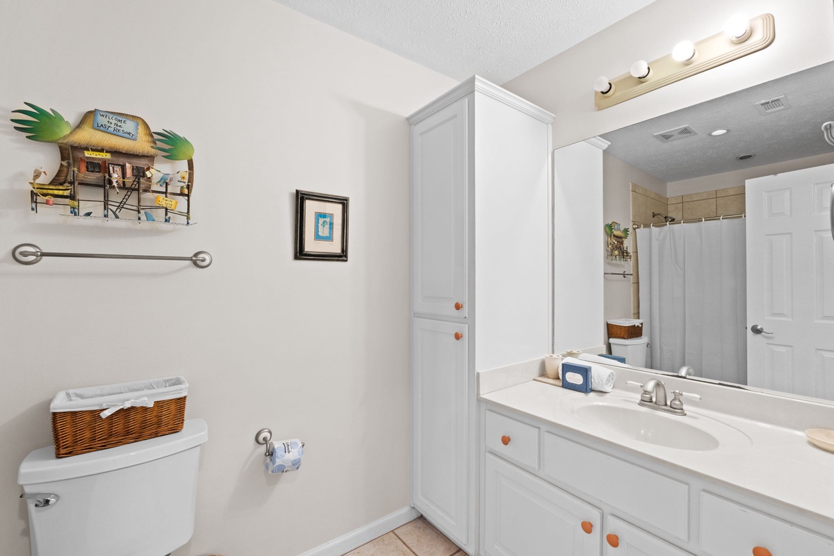 Your private bathroom features bright white cabinetry, ample storage, and cheerful beach-themed touches for a coastal getaway feel.