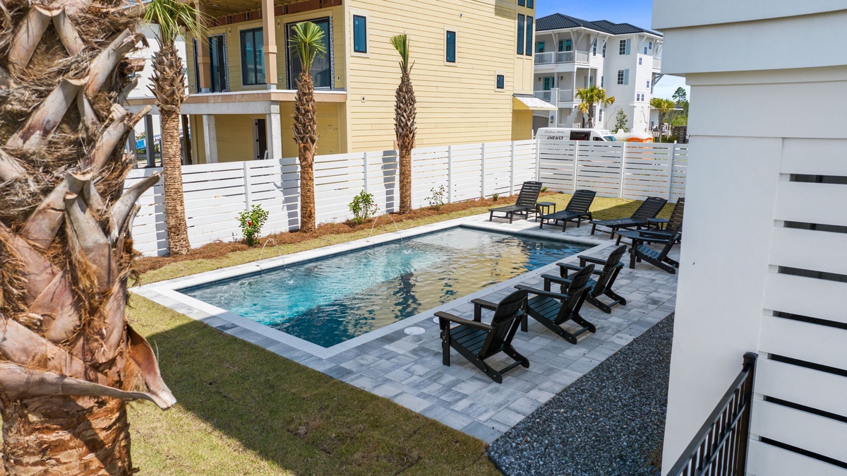 Modern backyard oasis featuring a sparkling pool surrounded by comfortable lounge chairs, lush landscaping with palm trees, and privacy fencing—perfect for sunny days and relaxation.