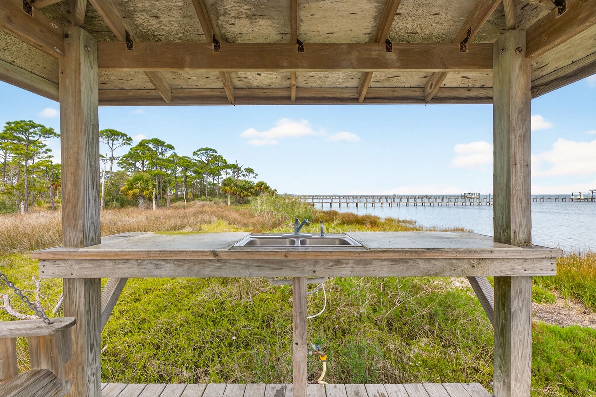 Rustic outdoor pavilion with sink overlooking serene waterfront and distant pier through coastal marshlands.