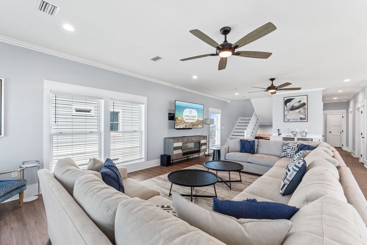 Unwind in this spacious living area with plush sectional seating, ceiling fans for comfort, and natural light from large windows. Your perfect spot for relaxing or gathering with loved ones.