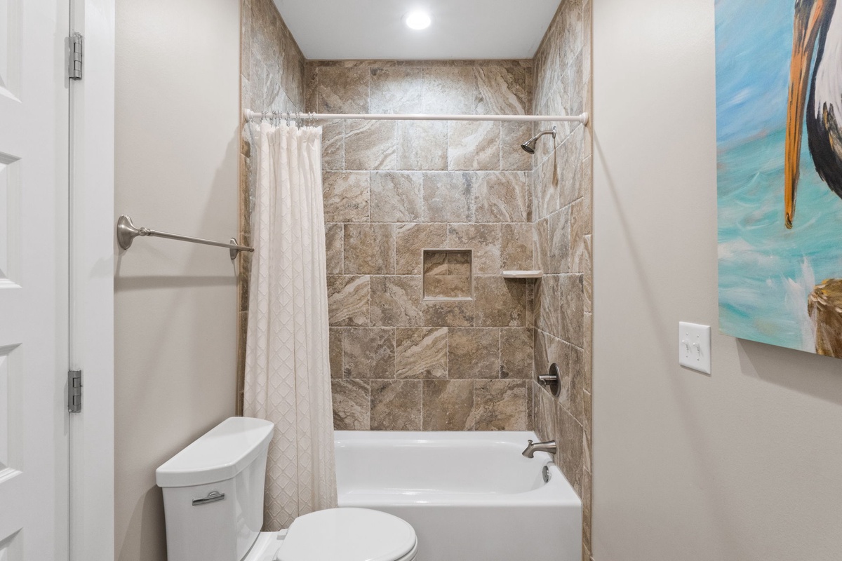 Refresh in your private bathroom featuring a spacious tub-shower combo with elegant marble-look tiling, modern fixtures, and coastal artwork for a relaxing retreat.