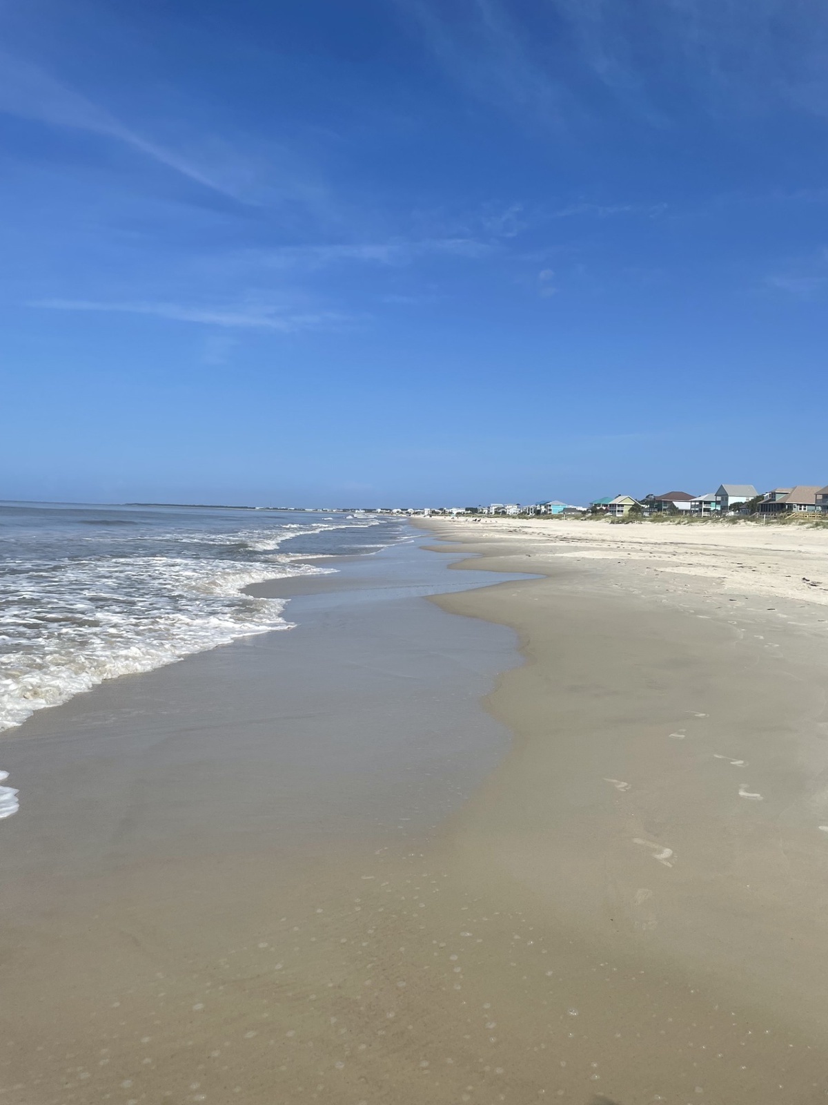 Pristine sandy beach stretches along the coastline with gentle waves and beachfront homes visible in the distance.