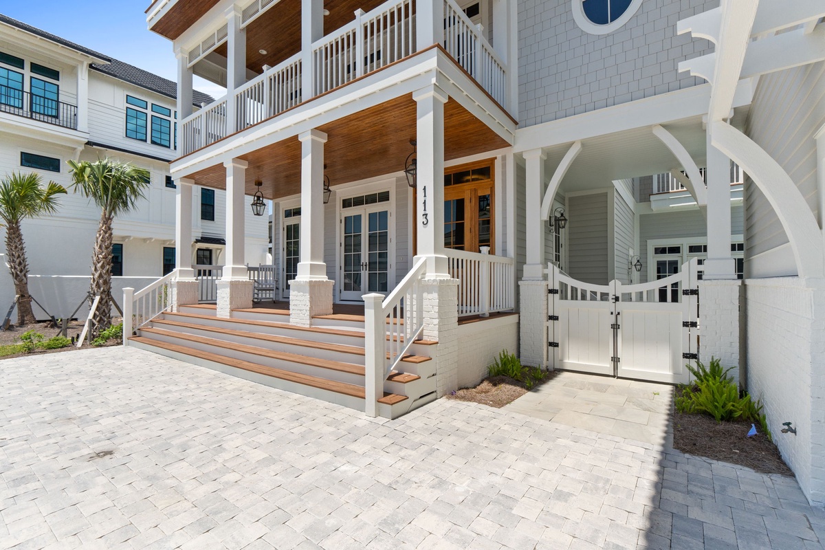 Coastal architecture showcasing the property's welcoming entrance with covered porches, white railings, and decorative elements framed by palm trees in the surrounding neighborhood.