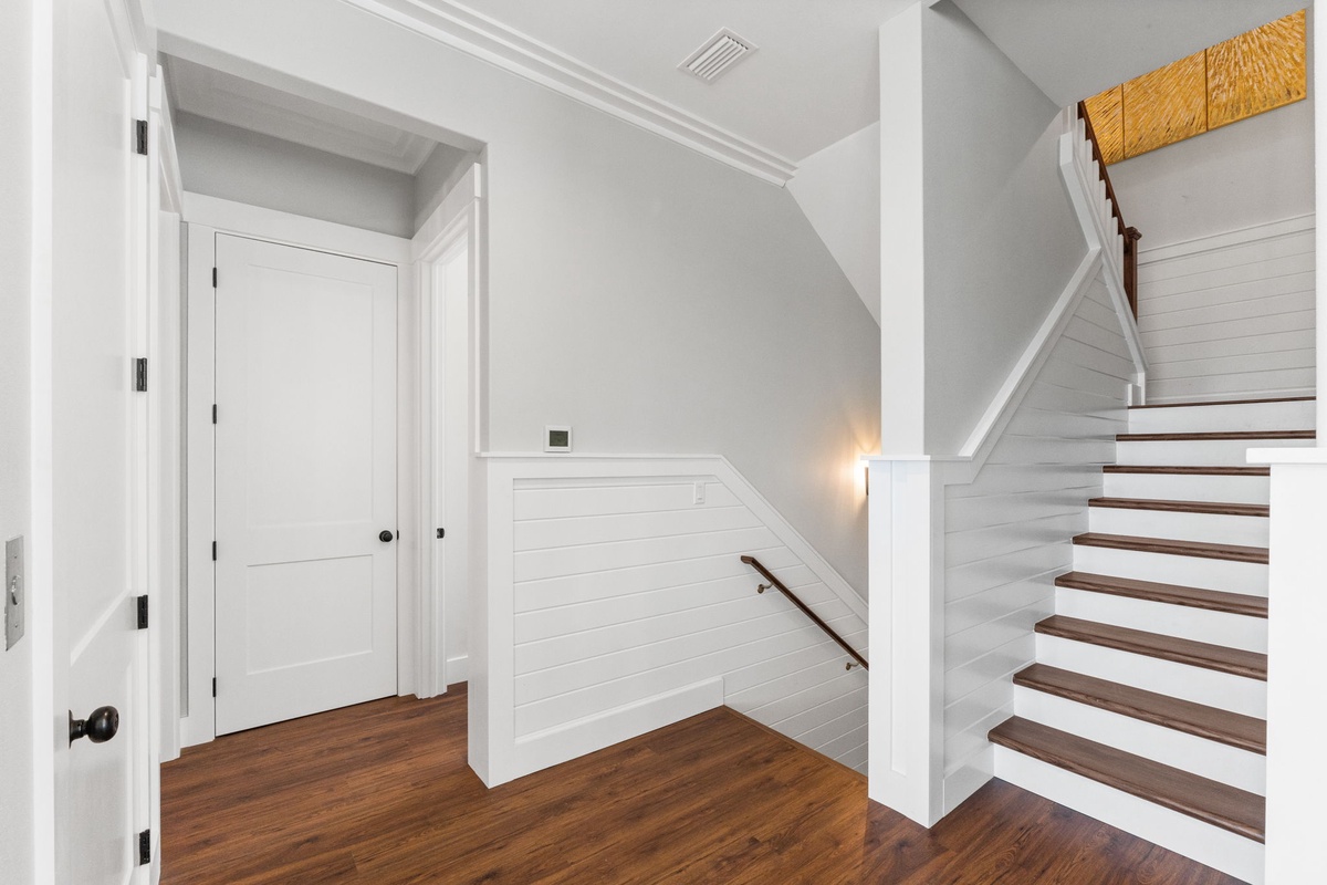 Elegant staircase with warm wood steps and classic white shiplap wainscoting creates a welcoming entrance to your upstairs retreat.