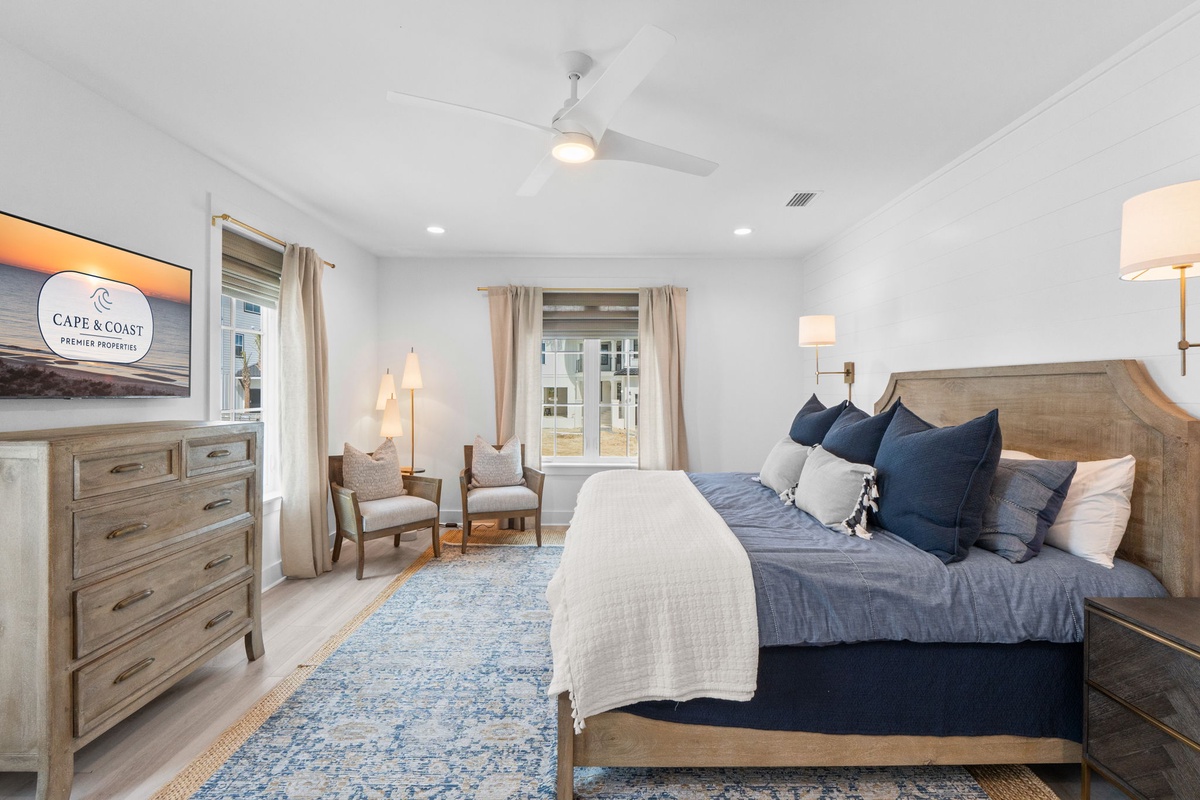 Unwind in your elegantly appointed bedroom featuring plush navy linens, coastal-inspired decor, and a peaceful seating nook by the window.