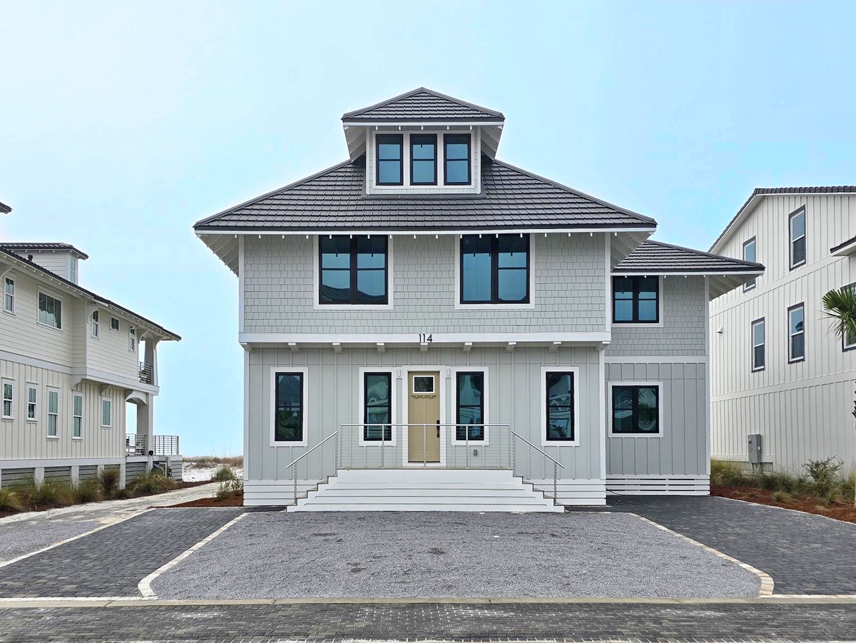 Modern coastal home featuring elegant gray shingle siding and inviting front entrance with convenient parking.