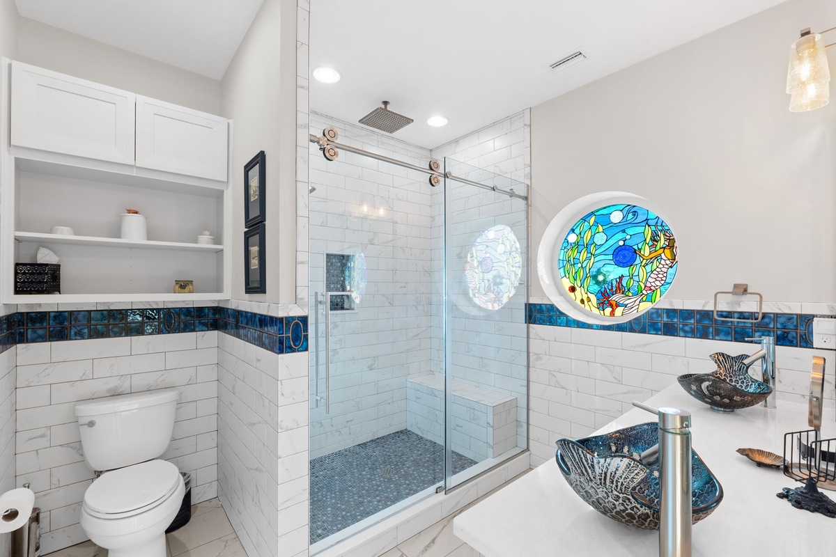 Indulge in your private spa-like bathroom featuring stunning ocean-themed glass art, a rainfall shower, and beautiful blue mosaic accents that transport you to tranquility.