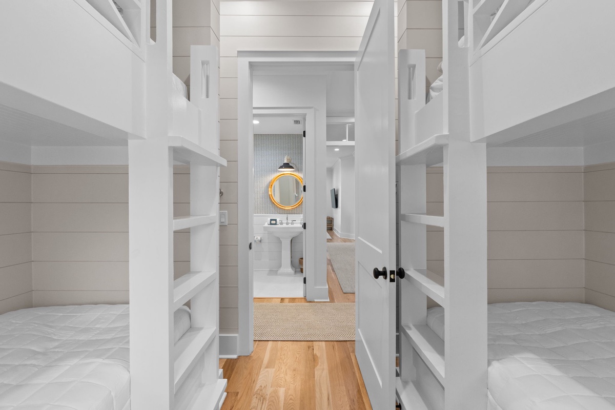 Cozy bunk room with smart built-in storage leads to your private en-suite bathroom, offering comfortable sleeping quarters and convenient access to fresh linens.