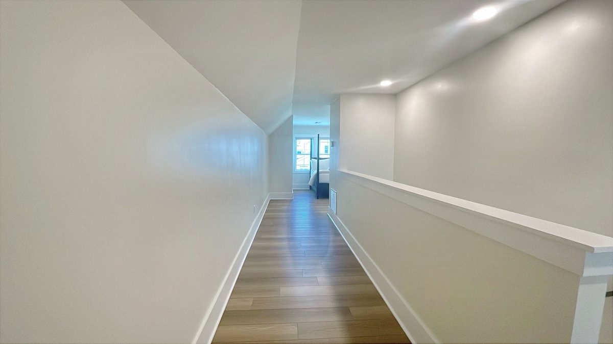 Modern hallway with sleek wood floors and soft lighting leads you seamlessly through your rental, connecting bright living spaces with a clean, contemporary feel.