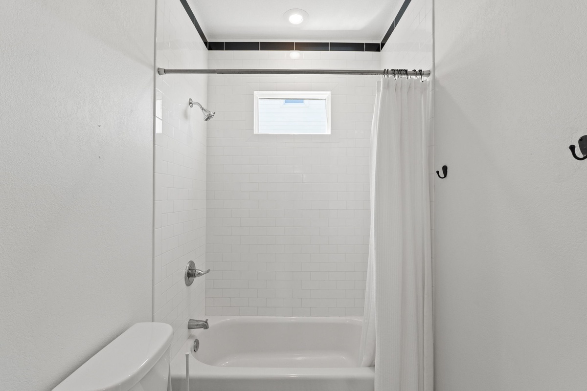 Step into your pristine bathroom featuring a full tub-shower combo with fresh white tiles and modern fixtures for your comfort.