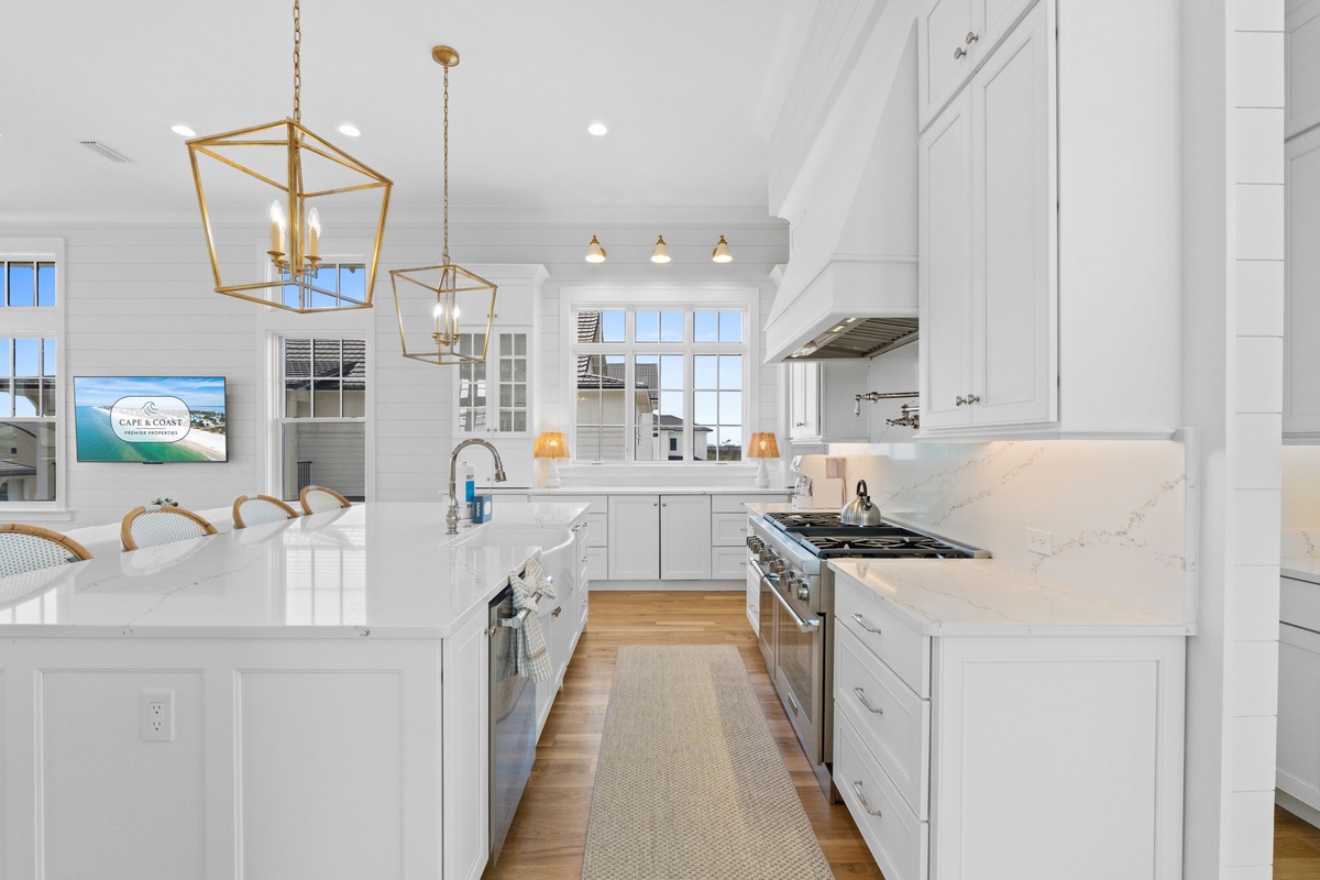 Bright, airy kitchen awaits with elegant white cabinetry, marble counters, and brass pendant lights. Your coastal escape begins here in this chef-inspired space.