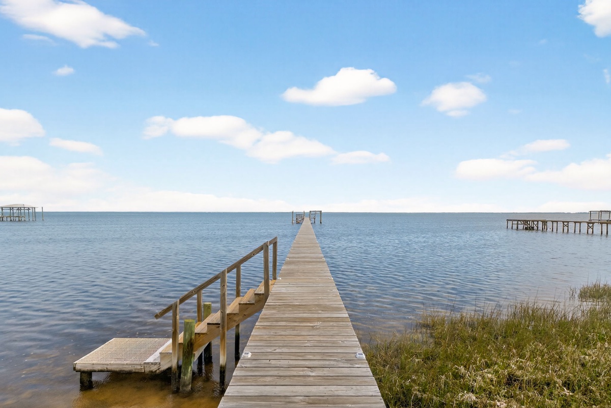 Peaceful waterfront setting with a private dock extending into calm waters under blue skies.