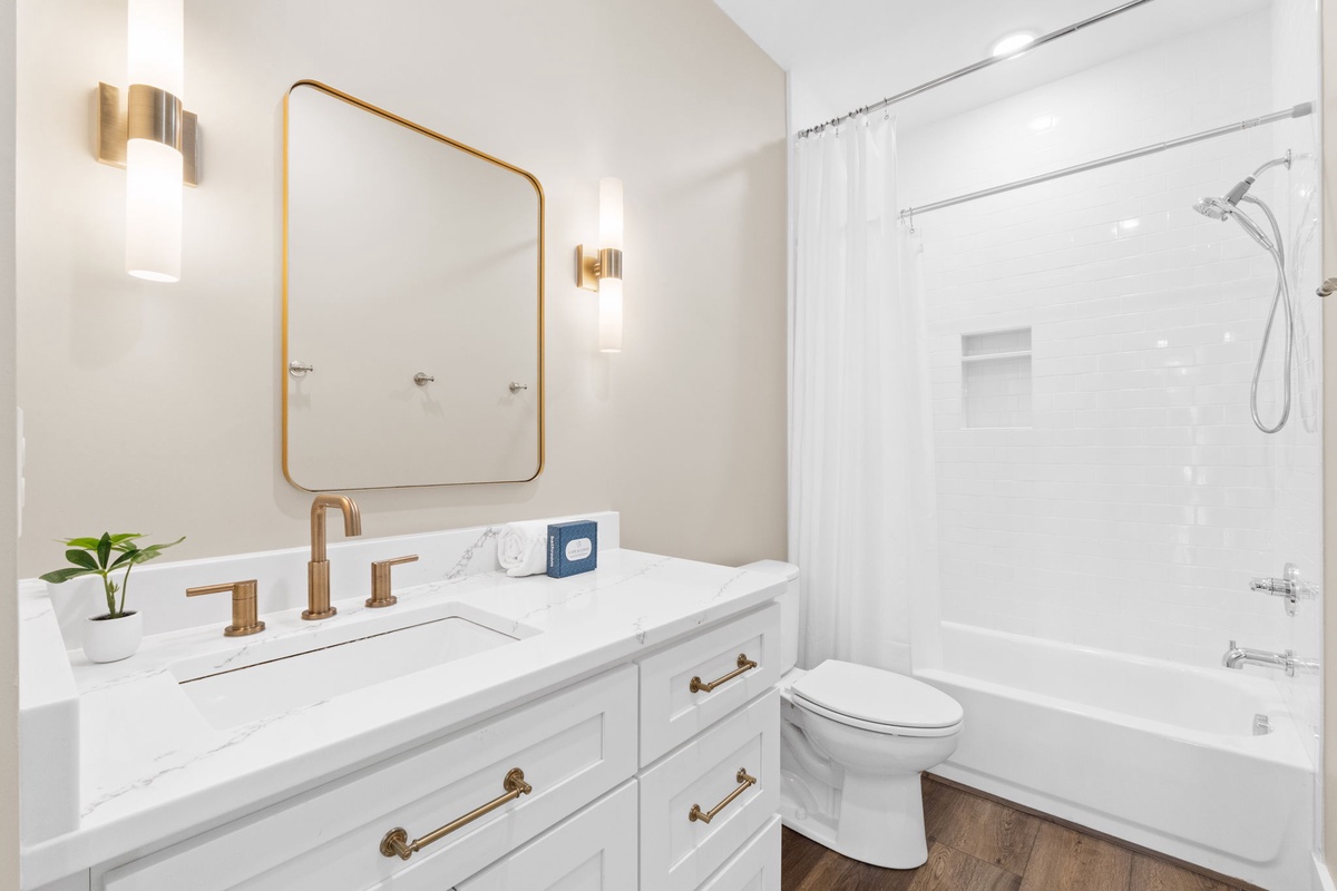 Step into your elegant bathroom featuring marble countertops, warm brass accents, and a pristine shower-tub combo for ultimate relaxation.