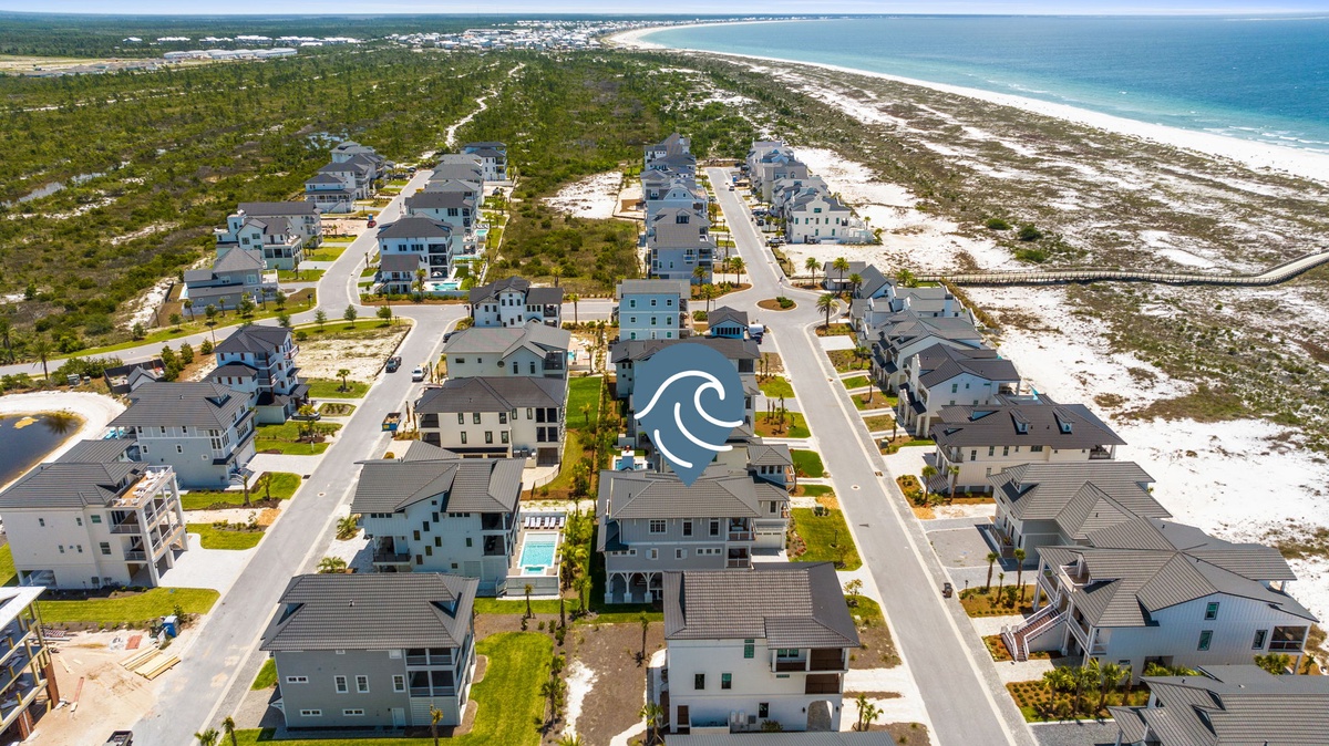 Aerial view of a coastal vacation rental community nestled between natural landscape and pristine beach, with ocean access just steps away.