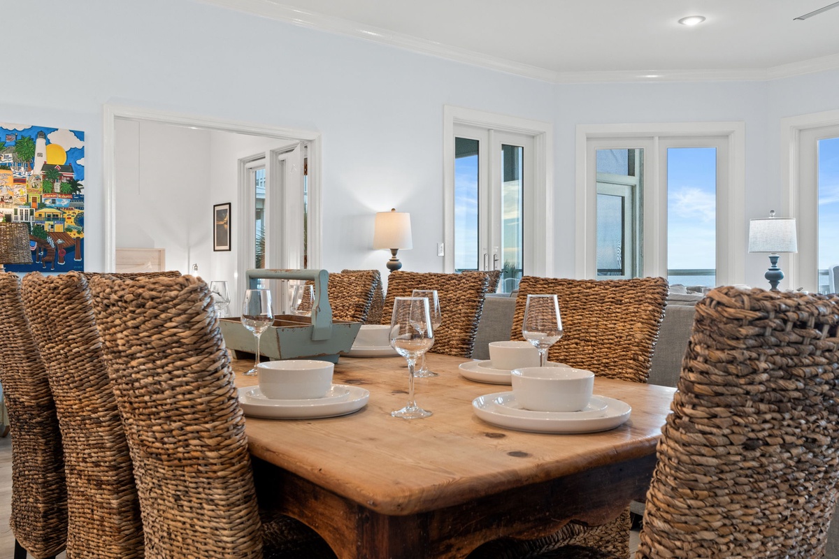 Gather around your elegant dining table with woven chairs, where ocean views through floor-to-ceiling windows create the perfect backdrop for memorable meals.
